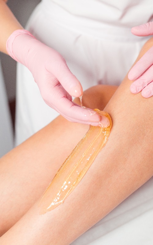 Frau bei der Enthaarung der Beine mit Zuckerpaste im Salon