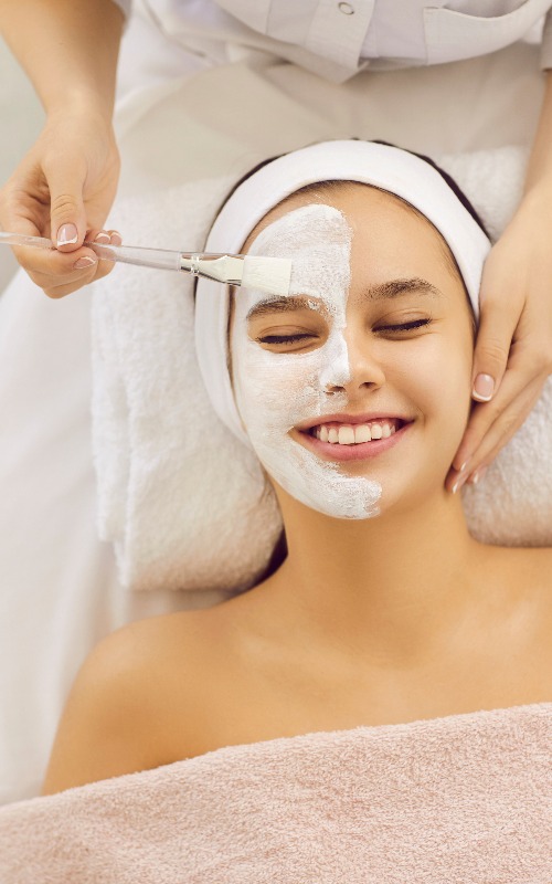Junge Frau genießt die Gesichtsmaske aus weißem Ton während einer Gesichtsbehandlung im Schönheitssalon