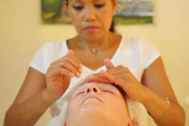 Eine Frau mit konzentriertem Gesichtsausdruck massiert das Gesicht eines liegenden Menschen